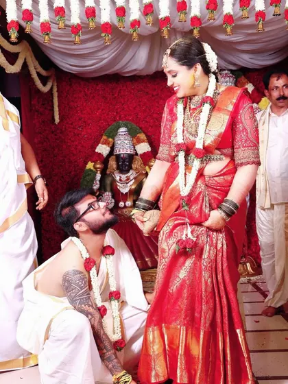 A candid moment from a wedding ceremony, with the bride looking beautiful in her red Kanjivaram saree and custom blouse.
