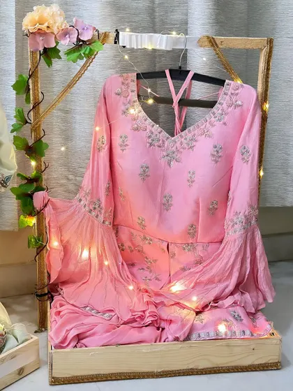 A stunning pink bridal outfit displayed on a custom stand adorned with fairy lights and ivy. This presentation style elevates the trousseau, making the outfit a centerpiece of the gift display.