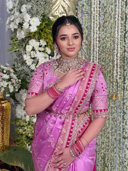 The bride stands against a beautiful floral backdrop, her radiant makeup and elegant saree creating a picture-perfect moment.