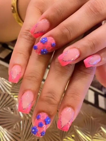 A vibrant and playful design with pink French tips outlined in silver glitter. The accent nails feature intricate 3D sculpted purple flowers for a fun, textured look.