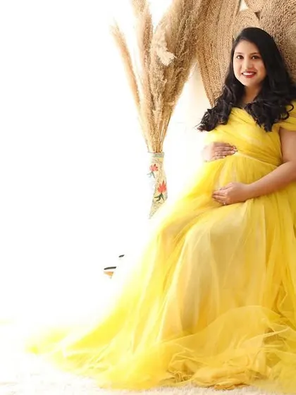 The light of new life. This mom-to-be shines in a yellow tulle gown, seated in a bright and airy boho-themed corner of the studio.