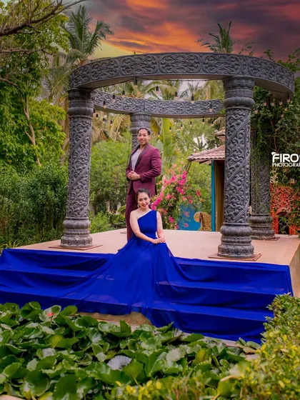 A majestic portrait at sunset. The couple is posed on the steps of the stone structure, with the dramatic blue gown cascading down, creating a regal and cinematic feel.