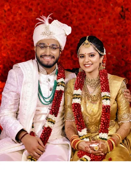 A vibrant portrait of a smiling couple against a rich red floral backdrop, perfect for a wedding album.