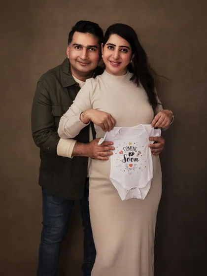 A joyful announcement portrait. This couple holds up a "Coming Soon" onesie, sharing their excitement in a classic, beautifully lit studio setting.