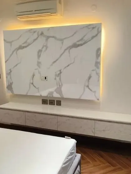 A minimalist TV unit in the bedroom, featuring a floating console and a large marble panel with backlighting. This creates a clean, sophisticated look without taking up floor space.