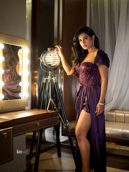 A full-length shot showing the complete look in a real setting. The vanity mirror and lights add context and a touch of backstage glamour to this event portrait.