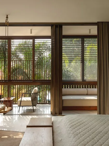 The bedroom opens onto a balcony veiled in operable timber lattices, a modern 'jaali' that provides privacy and diffuses the harsh sunlight, creating a constantly changing pattern of shadows within.