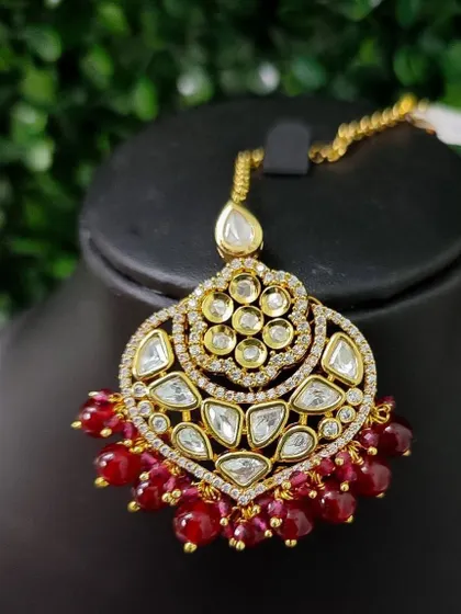 A beautiful kundan maang tikka with a heart-shaped design and rich red bead drops. A perfect accessory for a romantic bridal look.