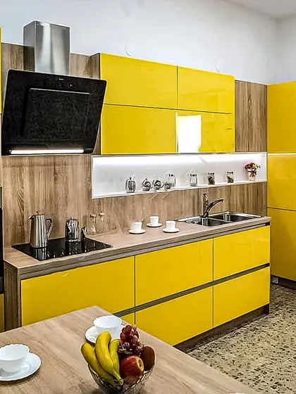 A vibrant and cheerful modular kitchen design featuring bright yellow handleless cabinets paired with a warm wood-grain finish. This layout includes a built-in oven and chimney, ensuring full functionality in a compact space.