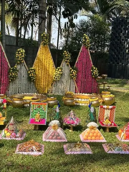 An outdoor setup for a traditional ceremony. The decorations include floral cones and individually decorated platters laid out on the grass, creating a beautiful and unique garden theme.