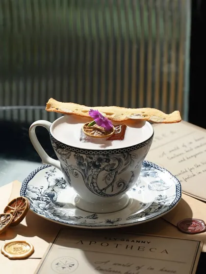 A closer look at the Breakfast Bramble, served in a delicate, vintage-style teacup and saucer, garnished with a dried citrus wheel and an edible flower.