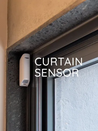 A curtain sensor installed on the frame of a sliding glass door. This discreet device provides an invisible layer of protection, perfect for securing large openings without obstructive hardware.