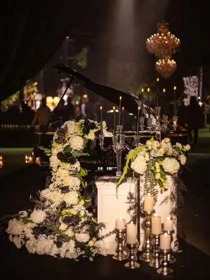 A grand piano becomes a stage for a cascading floral installation. This dramatic arrangement of white and black flowers, accented by elegant candelabras, served as a stunning focal point for the evening's entertainment.