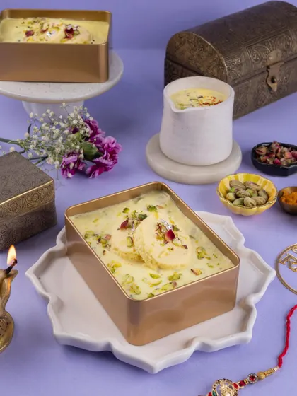 A three-quarter view of the Rakhi Rasmalai, showcasing the dessert alongside a traditional diya and gift boxes for a complete festive story.