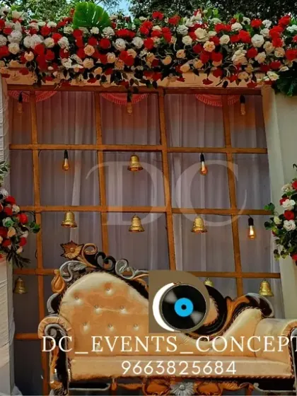 A beautiful outdoor Mehendi stage setup with a backdrop of red and white florals. The elegant draping and hanging bells add a traditional touch to the bright and airy design.