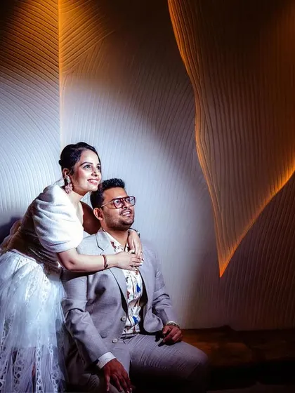 An artistic, dramatically lit portrait. The couple is posed against a textured wall, with light creating beautiful patterns and highlighting their forms.