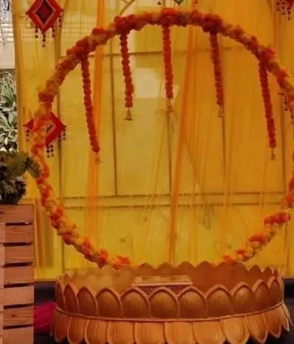 A modern Haldi setup with a circular marigold frame, "HALDI" foil balloons, and a traditional 'urli' on a patterned rug.