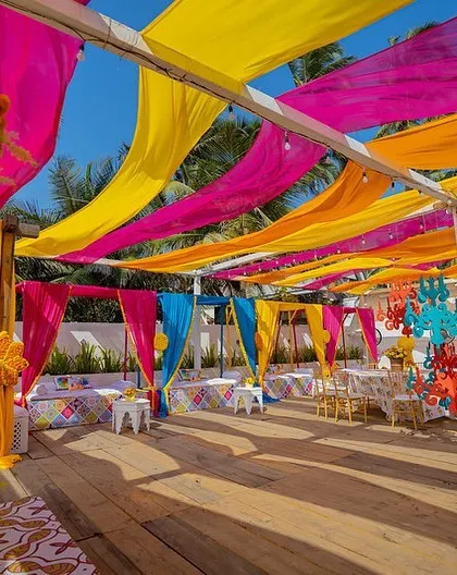 A vibrant Haldi setup with a canopy of colourful drapes and quirky chandeliers, perfect for a beachside celebration.