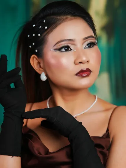 A vintage-inspired look with sharp graphic eyeliner dotted with pearls. The hair is styled in a sleek ponytail, and the entire look is completed with classic black gloves.