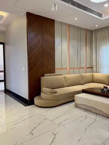 An L-shaped sofa provides ample seating in this living room, with a custom wood-paneled wall adding texture and warmth. The design balances modern aesthetics with functional comfort.