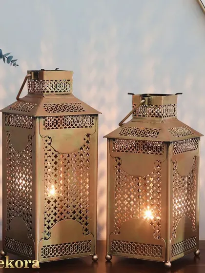 A pair of golden metal lanterns with intricate latticework. Inspired by Moroccan design, these holders cast beautiful shadows and add a warm, exotic touch to any space.