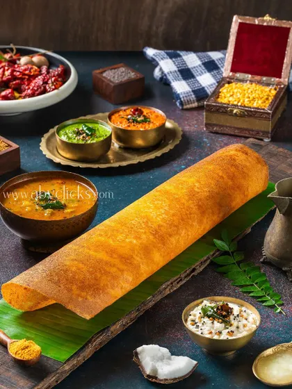 A perfectly crisp and golden-brown masala dosa, presented on a banana leaf with an array of colorful chutneys and sambar.