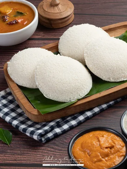 Soft, fluffy idlis served on a traditional banana leaf. I used dark, warm lighting to create a comforting and authentic South Indian breakfast scene.
