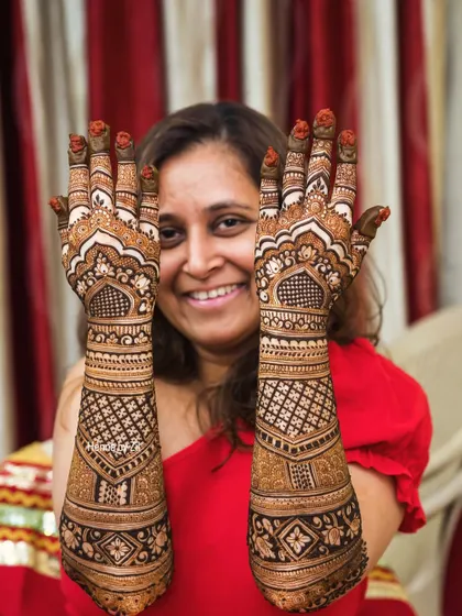 A happy bride showcasing her full, traditional bridal mehendi. The design is dense with geometric patterns and classic motifs.