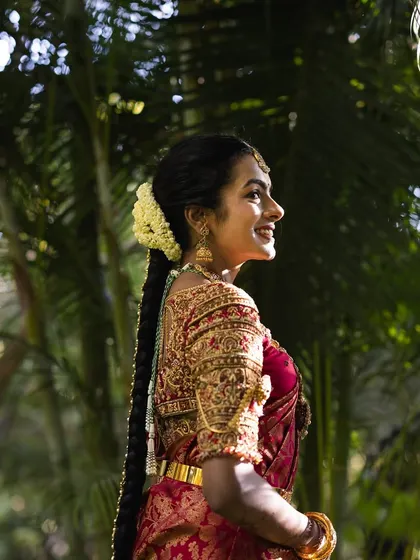 The smile of a happy bride is everything. This candid shot captures her joy, framed by the exquisite zardozi work on her red silk blouse and the traditional flowers in her hair.
