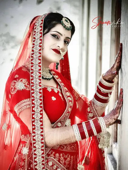 A vibrant portrait of a bride in a bright red lehenga, her pose full of confidence and style.