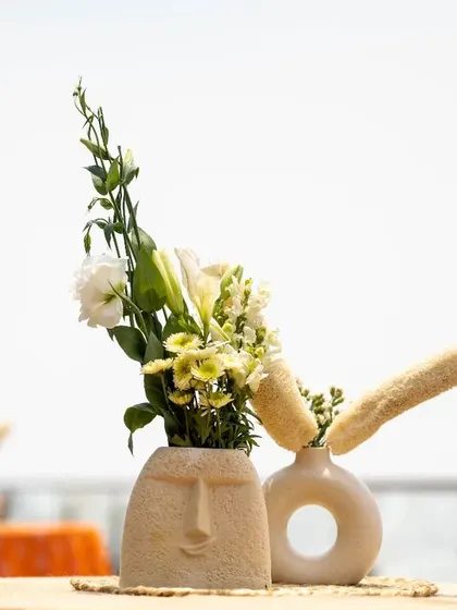 A quirky and artistic centerpiece. This setup features a vase with a face motif and a modern, donut-shaped vase, showcasing our love for unique and creative details.