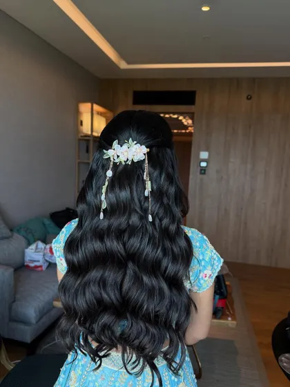 A modern and fresh half-updo with long, flowing waves. The look is completed with a delicate floral hairpiece, perfect for a daytime wedding or Mehendi.