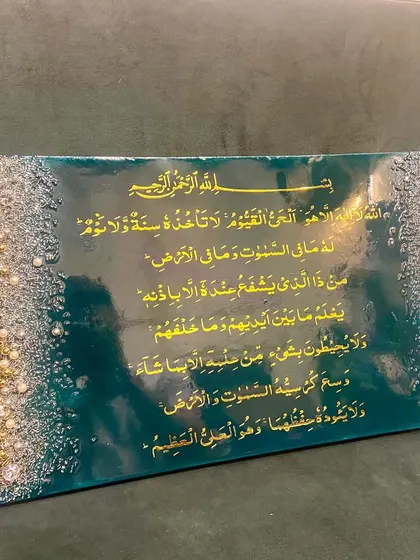 A rectangular Ayat al-Kursi piece in emerald green and gold, with textured borders of silver, gold, and pearls.