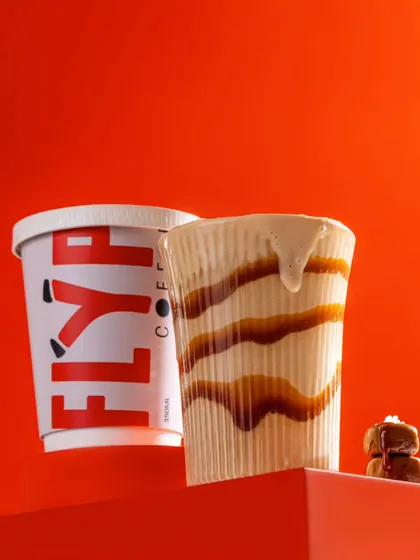 A creative shot of a caramel iced coffee from Flyp, with a dramatic drip down the side of the glass. The bold red background makes the image stand out.
