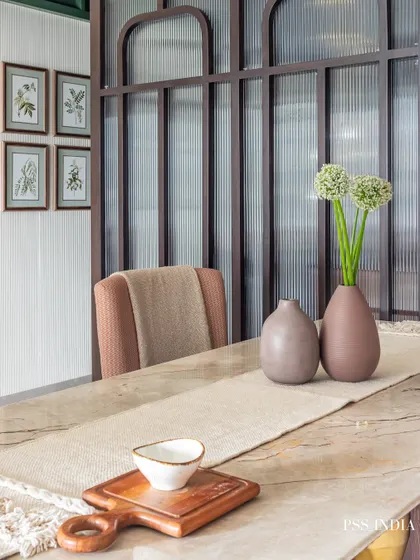 A close-up of a beautifully styled dining table. A simple linen runner, minimalist ceramic vases, and a wooden serving board create an earthy and inviting tablescape, complemented by fluted glass partitions in the background.