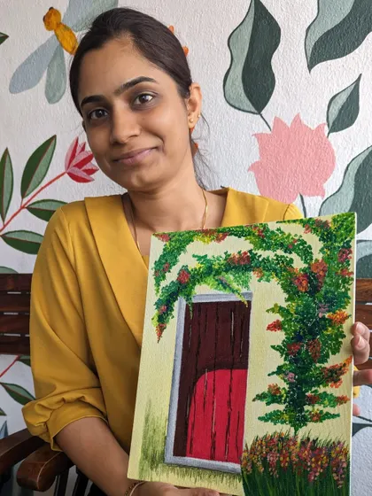 A participant proudly displays her finished canvas painting of a red door. The vibrant colors and charming subject make for a lovely piece of art.