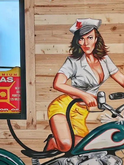 A closer look at the pin-up girl and the real gas can placed in a window cutout, blurring the line between the mural and the physical space.
