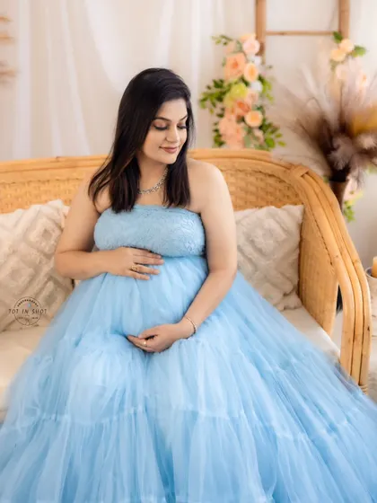 A peaceful solo portrait of a mom-to-be in a lovely light blue gown, seated on a cane sofa in our versatile studio.