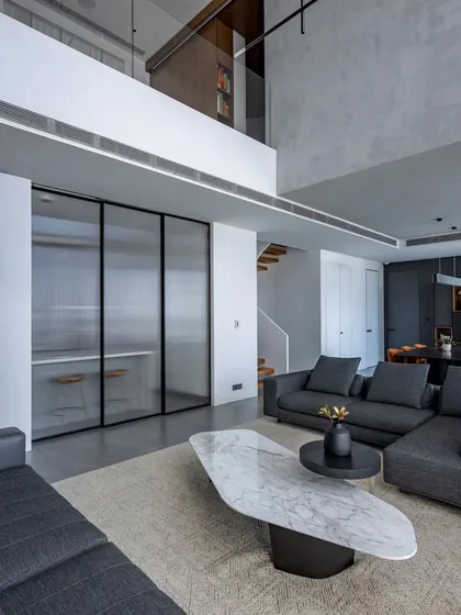 The living area of 'The Grey House', a duplex apartment in Mumbai. We embraced a minimalist aesthetic with a monochromatic grey palette, using textured walls and clean-lined furniture to create a space that is both sophisticated and calming. The double-height ceiling enhances the sense of openness and light.