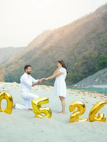 A romantic proposal-style photo on a beach, with the couple holding hands in front of balloons that spell out their wedding date.