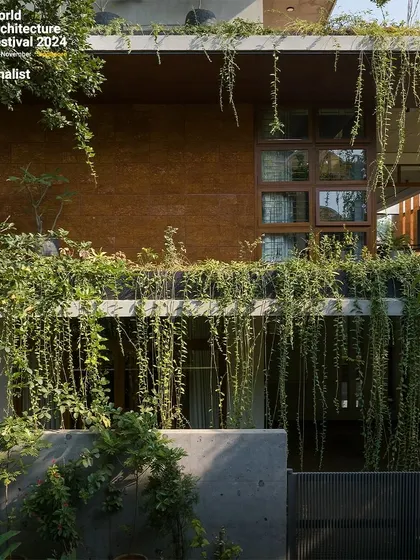 A close-up of the facade, showing the texture of the rammed earth wall and the curtain of green creepers.