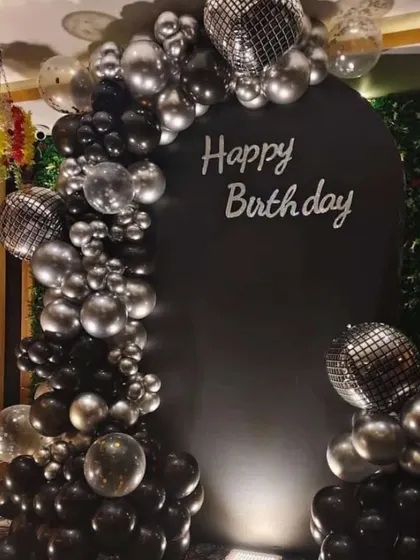 A sophisticated all-black birthday theme. This setup features a black balloon arch with silver and disco ball accents against a black backdrop.