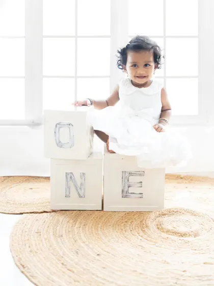 A classic first birthday portrait with "ONE" blocks. The baby girl's simple white dress and the natural light create a beautiful, timeless image.
