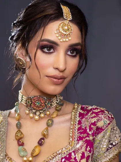 A close-up of a regal bridal look with a purple smokey eye and navratna jewelry. This showcases the skill of pairing colorful makeup with multi-toned jewelry.