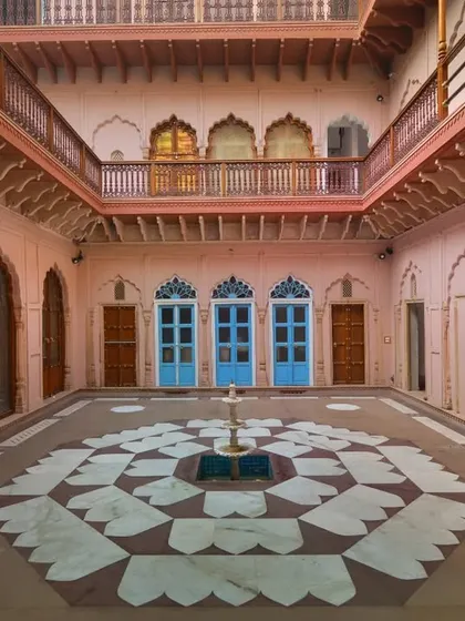 The restored courtyard features an octagonal flooring pattern and a central water fountain, inspired by traditional haveli design. This space allows for natural light and circulation throughout the entire structure.