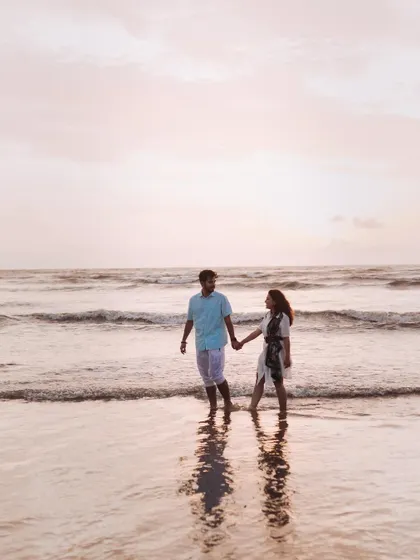 A quiet walk along the shoreline, hand in hand. The soft light and their reflection in the water create a peaceful and romantic atmosphere.