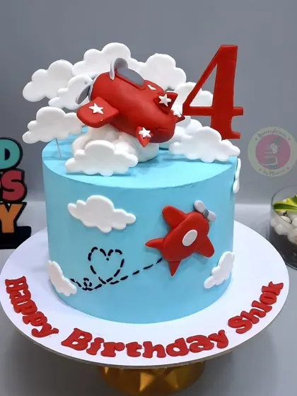 A simple and sweet airplane-themed cake, with a red plane flying through fluffy fondant clouds.