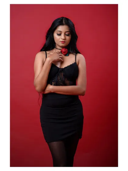 A full-length shot of a model in a black dress against a red background. The pose is strong and the color contrast is striking.