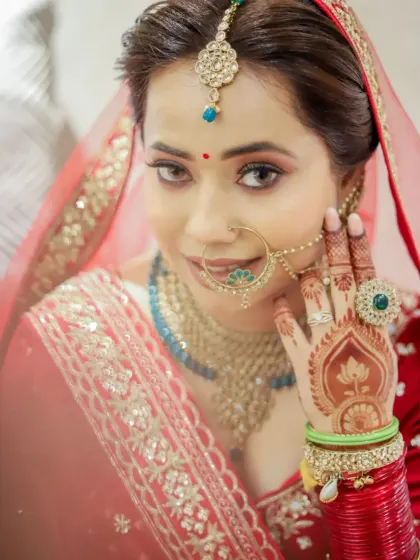 A close-up of a bride on her wedding day, with her mehendi-adorned hand framing her face.
