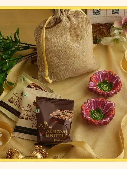 A close-up of the items in the yellow hamper, featuring almond brittle and two hand-painted diyas.